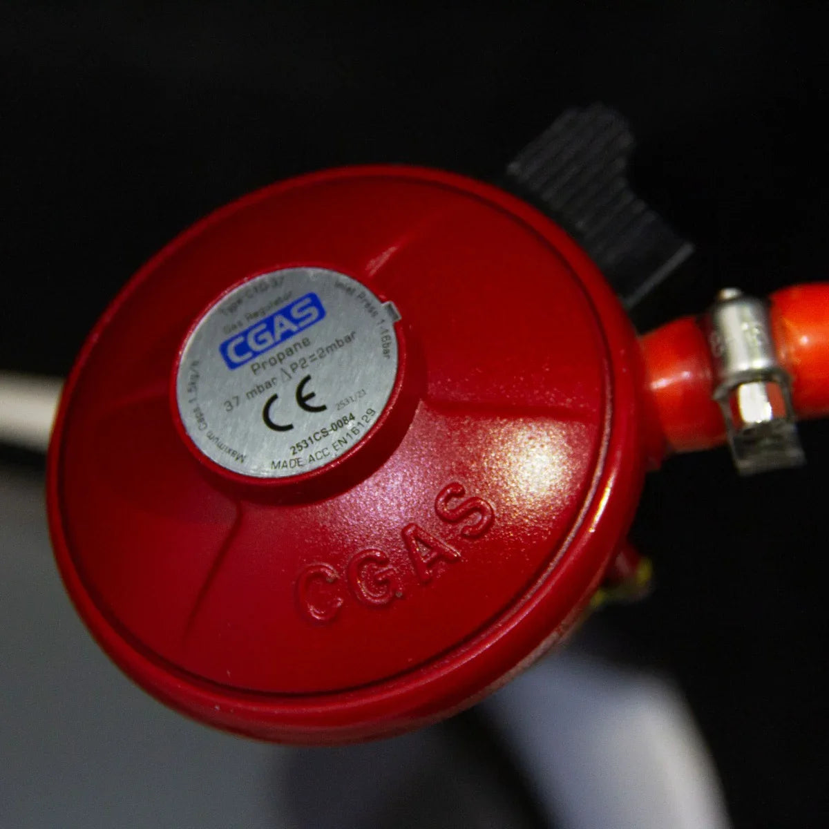 Red propane gas regulator with a silver label, designed for use with a stone gas fire pit heater, showcasing durable construction and secure fittings