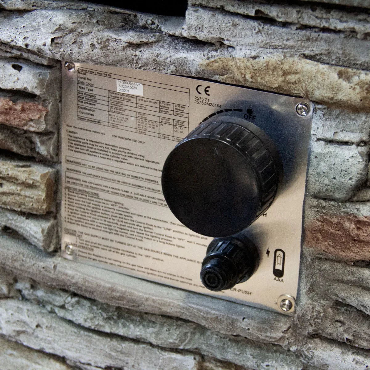 Control panel of a stone gas fire pit heater featuring a black knob, gas connection, and detailed safety instructions on a metallic plate