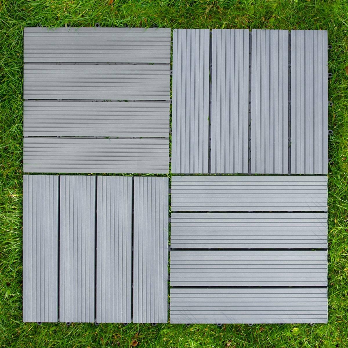 Grey WPC decking floor tiles, 30x30cm, featuring a textured surface with alternating slat patterns, arranged on green grass