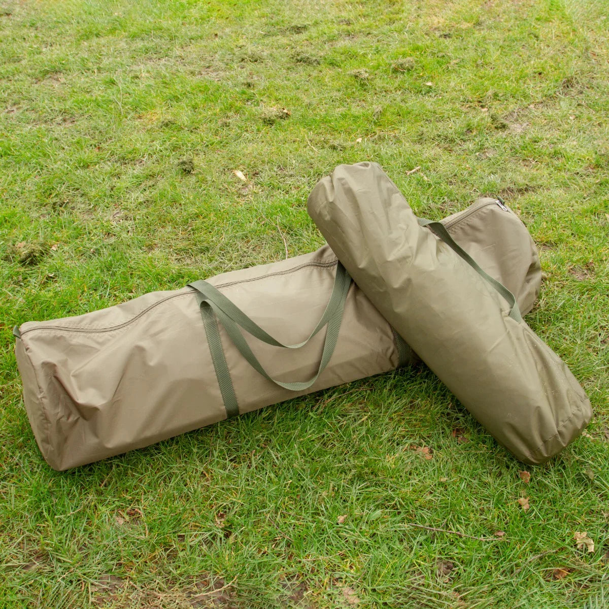 Two olive green fishing bivvy bags, one large and one smaller, resting on grass, designed for easy transport and setup