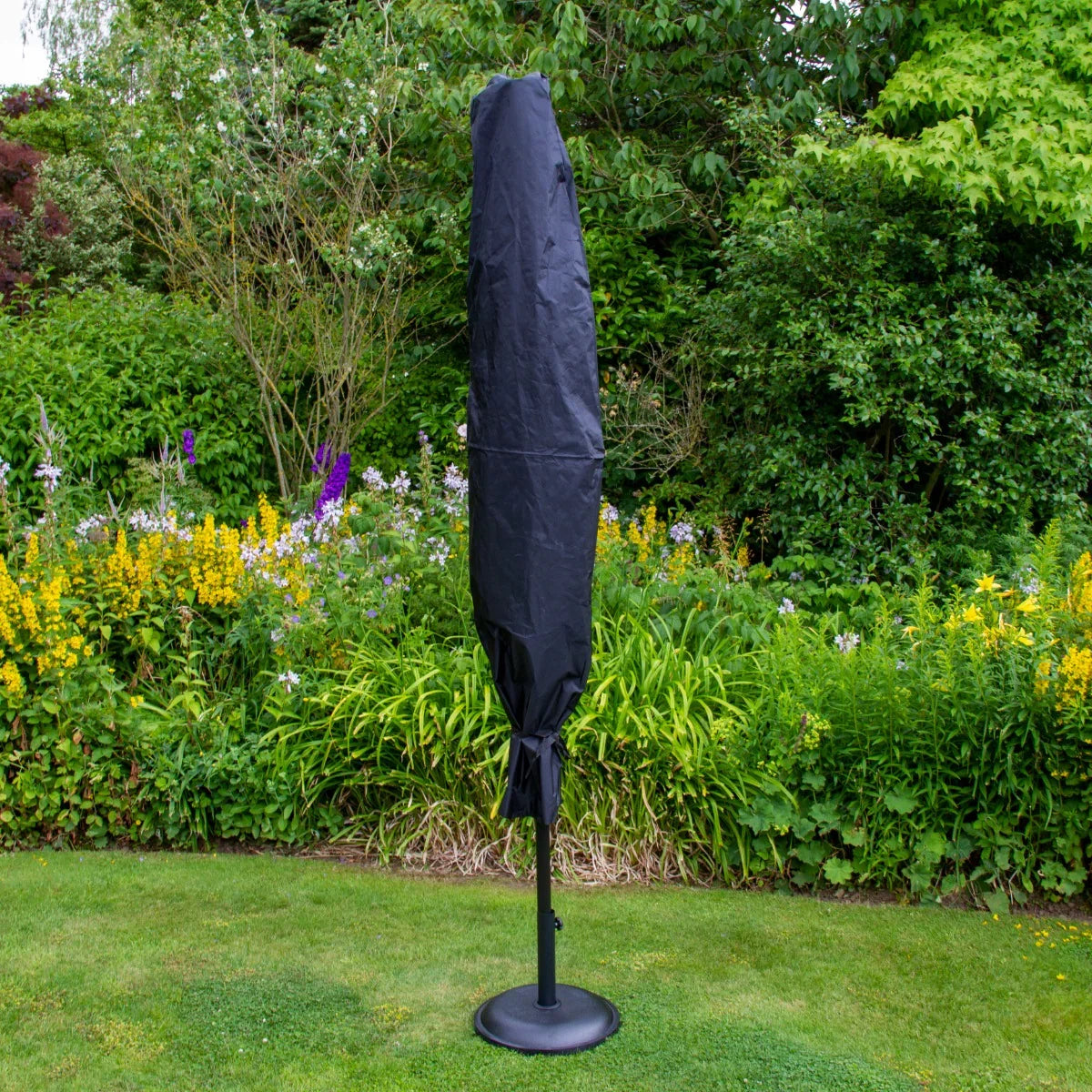Beige 2.7m LED tilt parasol with a sleek black cover, standing on a sturdy base, surrounded by vibrant garden flowers and greenery