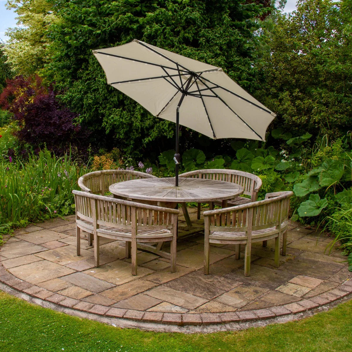 Cream 2.7m LED tilt parasol with a sturdy black frame, providing shade over a round wooden table and chairs in a lush garden setting