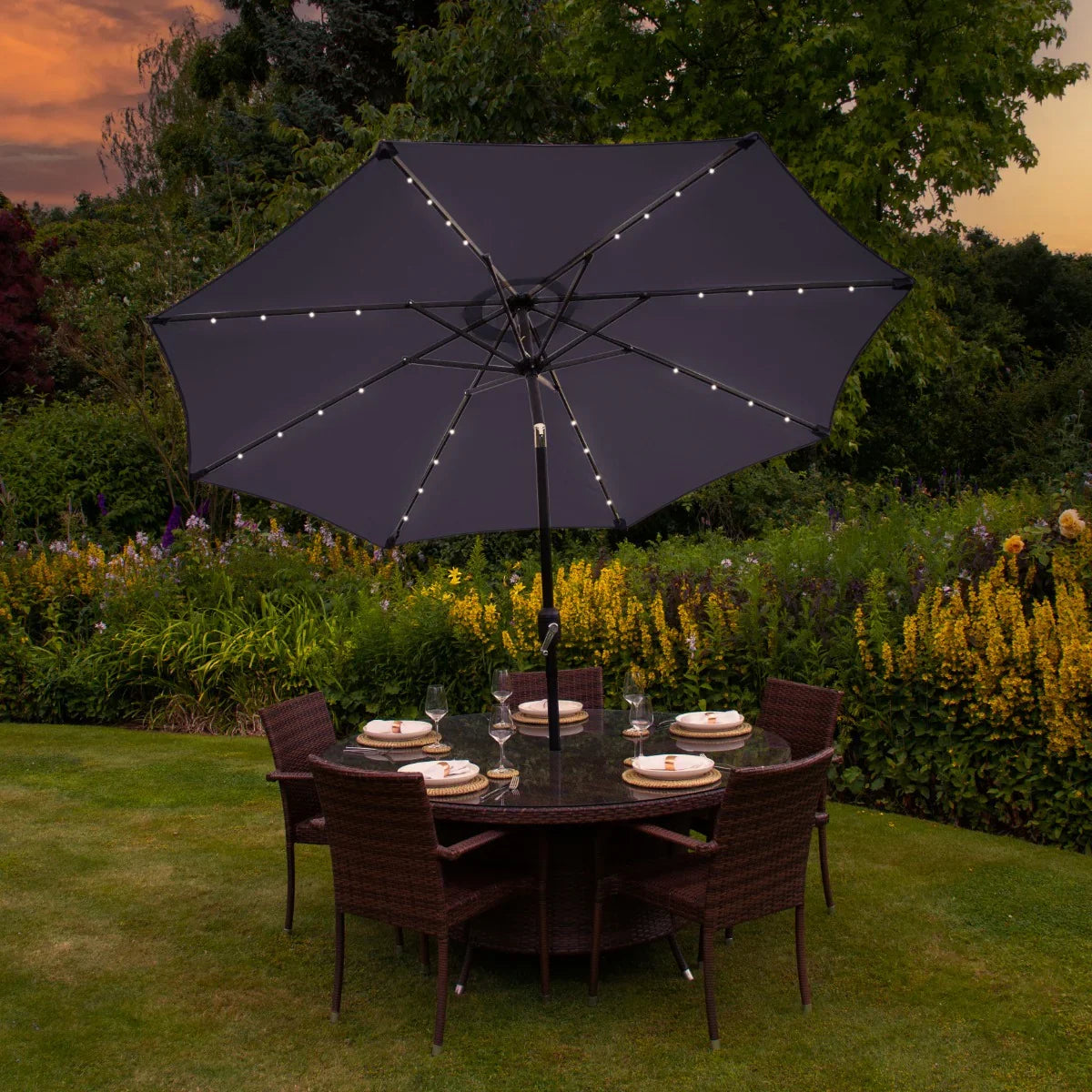 Grey 2.7m LED tilt parasol with warm lights, set over a round dining table surrounded by wicker chairs in a garden setting
