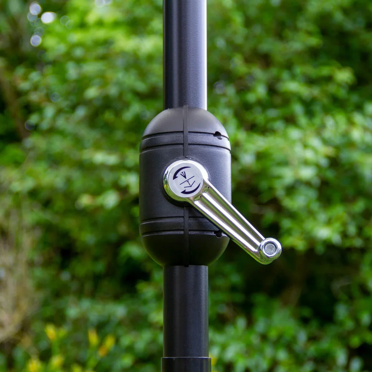Close-up of the grey LED tilt parasol's crank mechanism, featuring a sleek black design and shiny silver handle against a lush green background