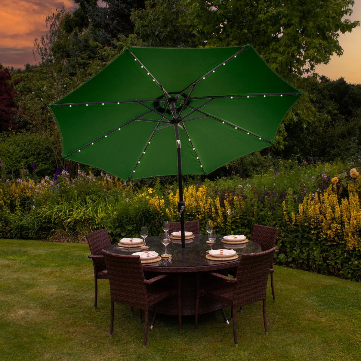 Green 2.7m LED tilt parasol with string lights, set above a round dining table surrounded by wicker chairs in a garden setting