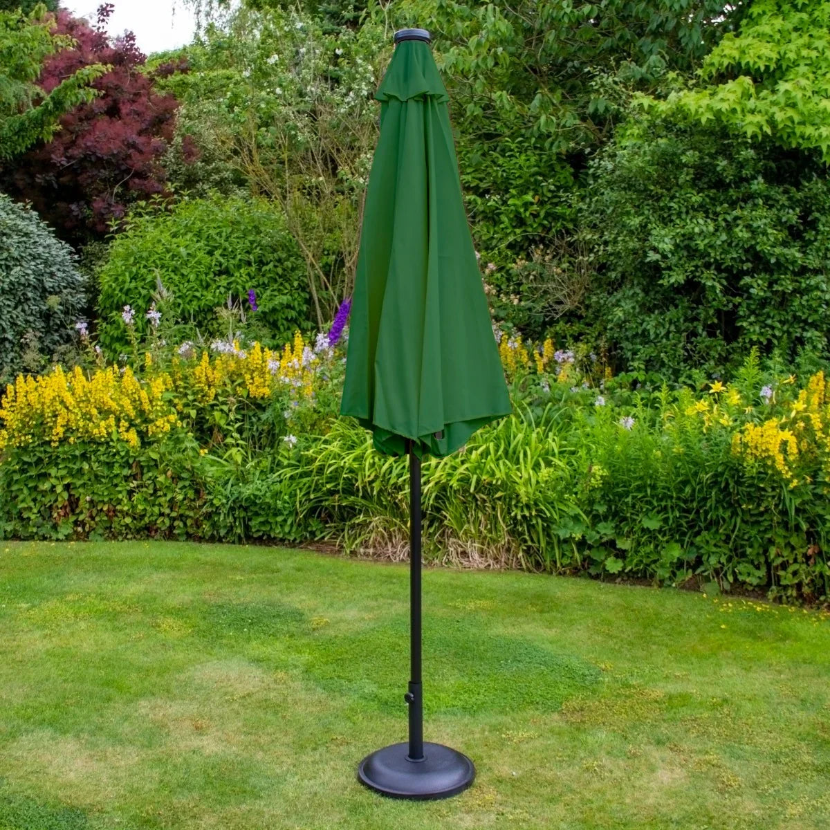Green 2.7m LED tilt parasol with a sleek black base, standing in a garden surrounded by vibrant flowers and greenery
