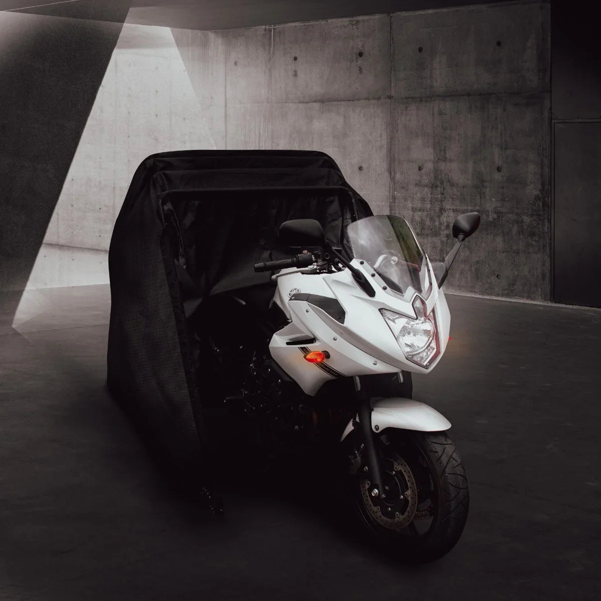 Black motorbike tent partially covering a sleek white motorcycle, showcasing its aerodynamic shape and protective design against elements