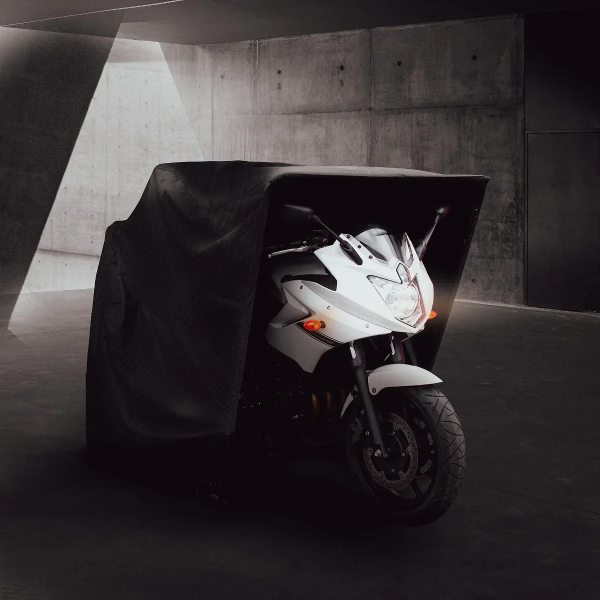 Large motorbike tent in black fabric, partially covering a sleek white motorcycle, showcasing a modern, protective design in a minimalist setting