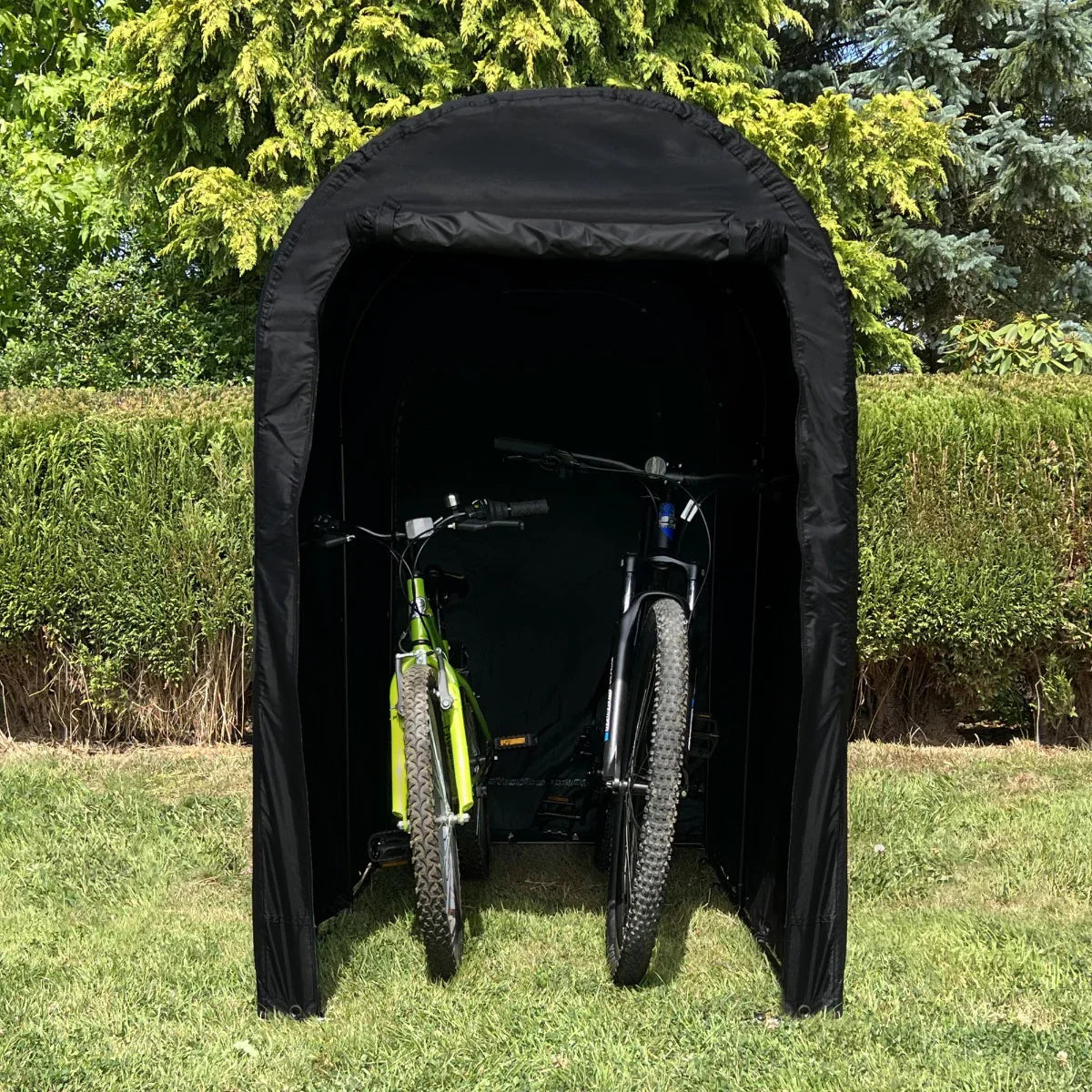 Waterproof bike tent in black, featuring a rounded top, securely housing two bicycles on a grassy area with greenery in the background