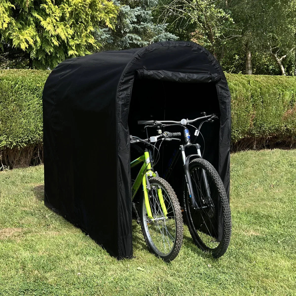 Waterproof bike tent in black, featuring a rounded top, sheltering two bicycles on grass with lush greenery in the background