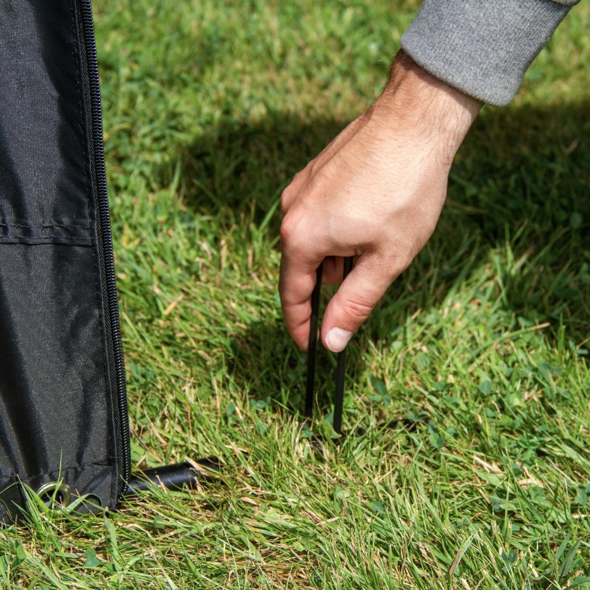 Hand securing a large black bike tent stake into green grass, showcasing durable material and easy setup for outdoor use