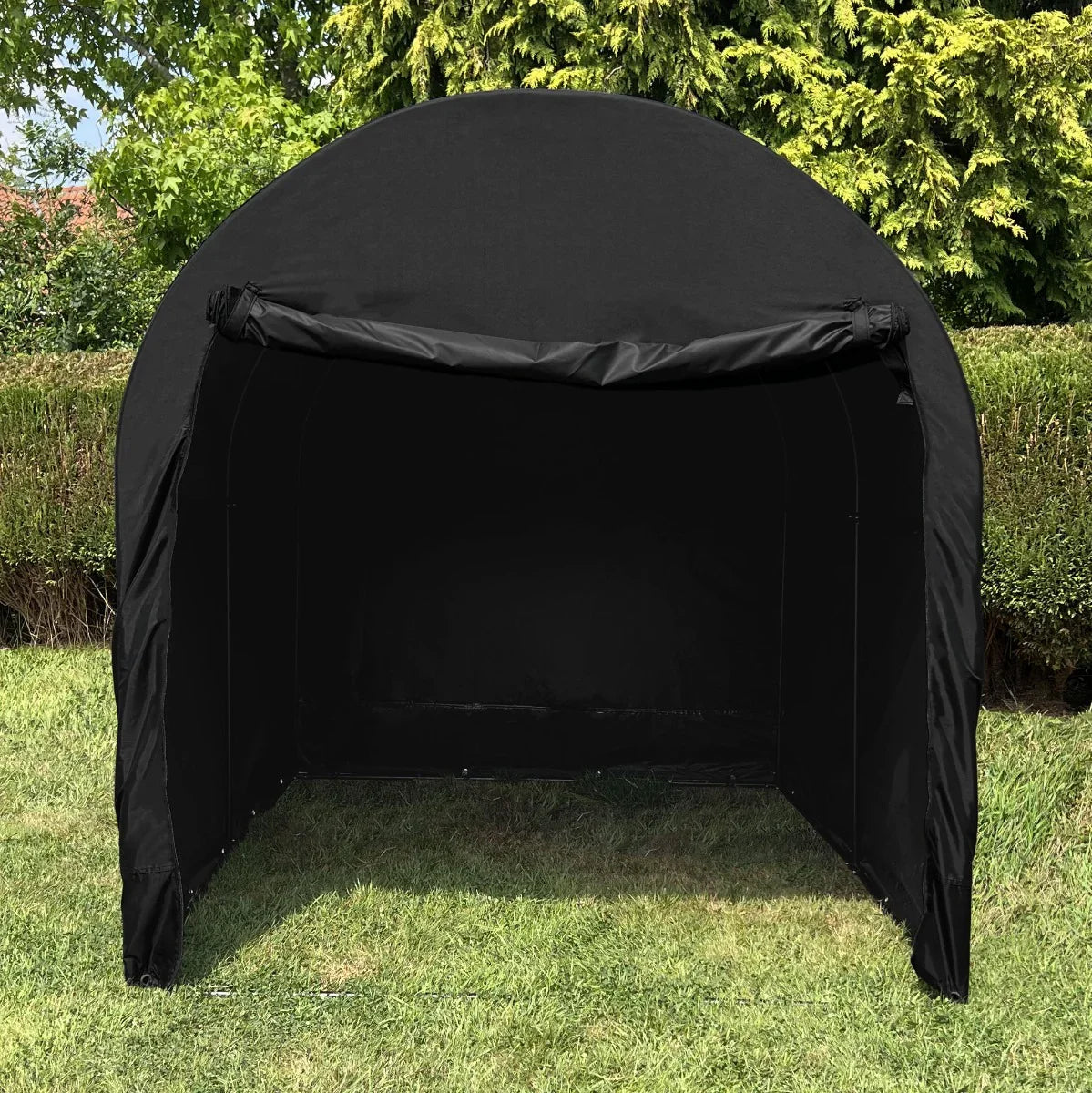 Large black bike tent with a spacious interior, featuring a rounded top and open front, set against a green hedge background