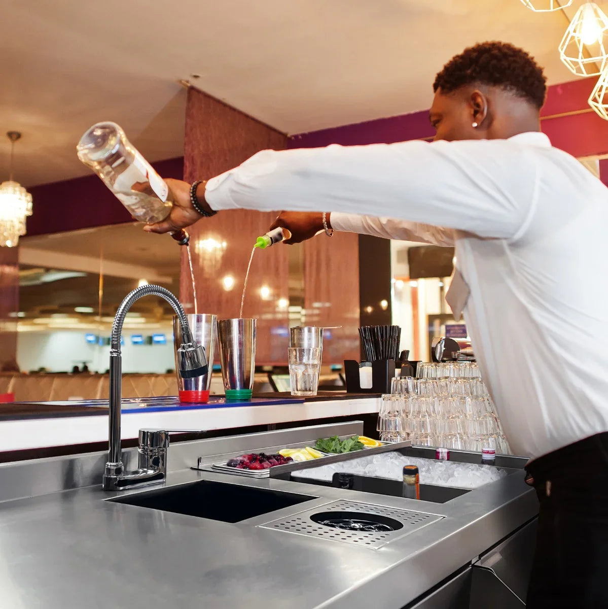 Deluxe Cocktail Bar Station with sleek stainless steel finish, bartender pouring drinks into shaker, fresh ingredients visible