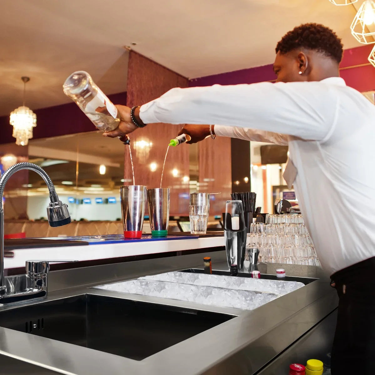 Cocktail bar station featuring a sleek black countertop, ice-filled basin, and a bartender mixing drinks with stainless steel shakers