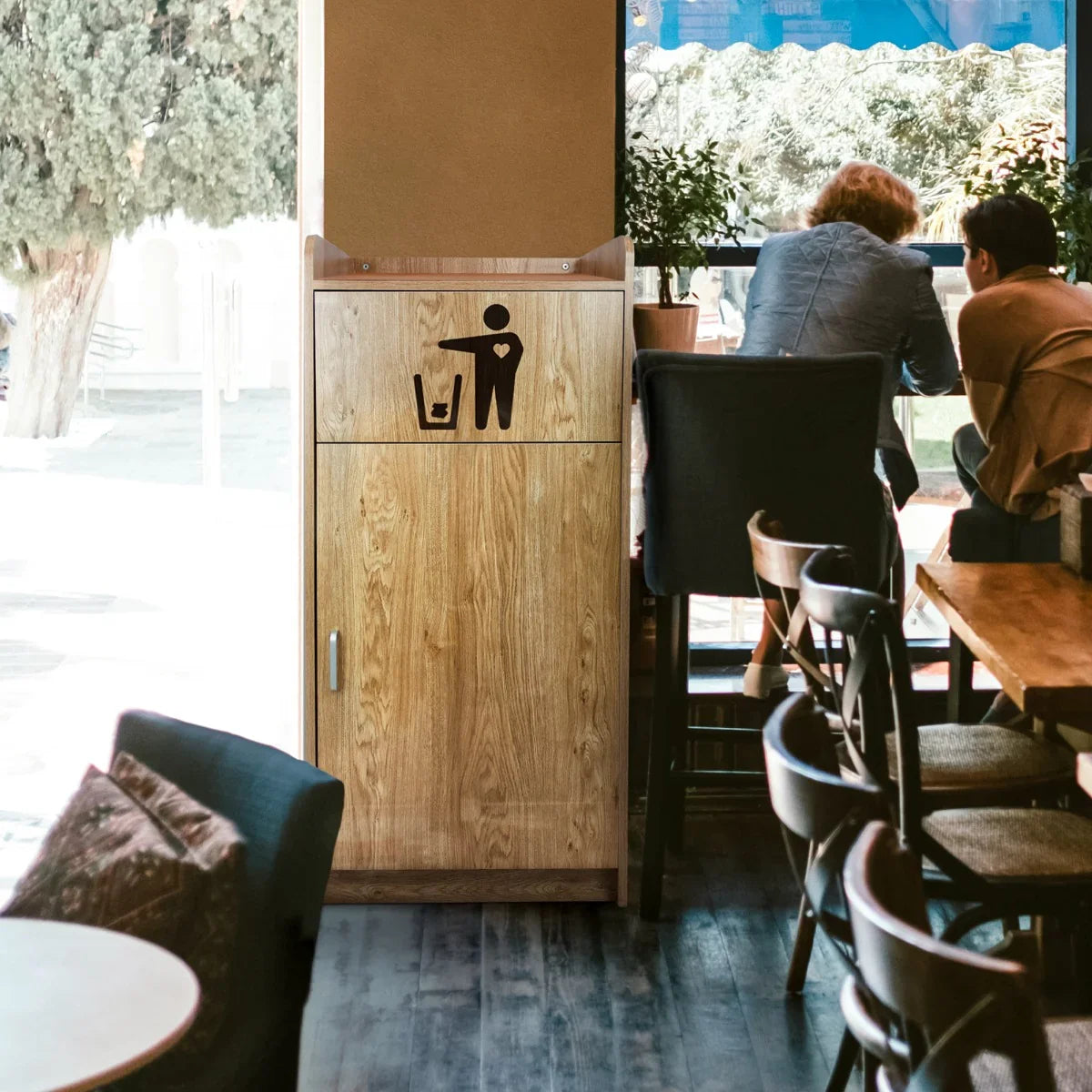 Light oak wooden litter bin and tray stand with a minimalist design, featuring a trash icon, placed in a cozy café setting