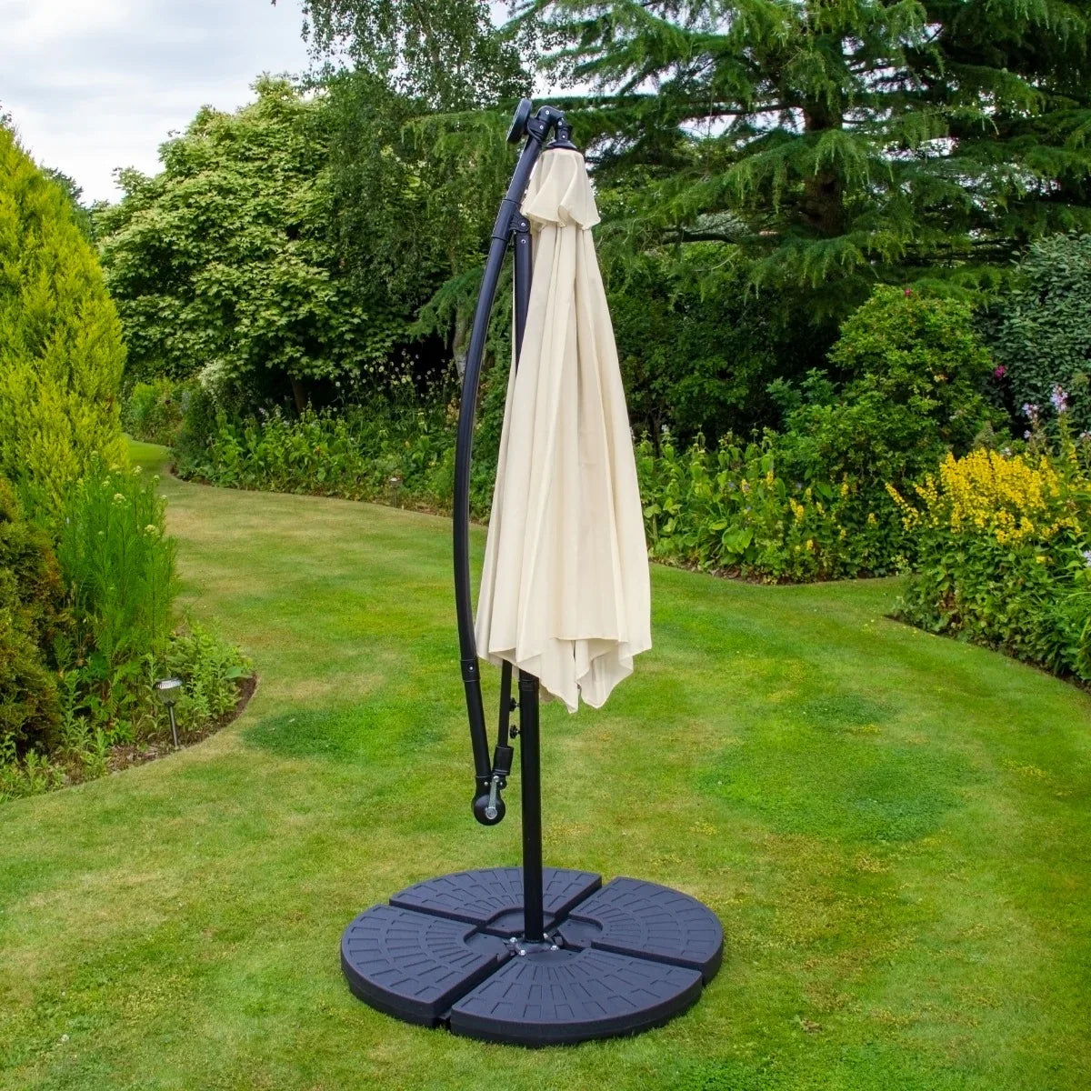Cream 3m LED cantilever parasol with a sturdy black fan base, elegantly curved arm, and soft fabric canopy, set in a lush garden