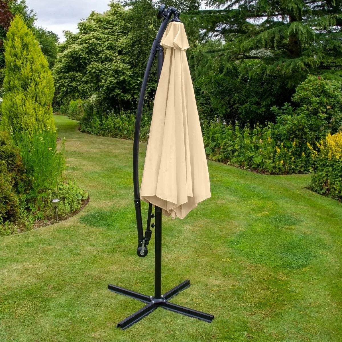 Beige 3m LED cantilever parasol with a curved frame, standing on a sturdy black base, set in a lush garden backdrop