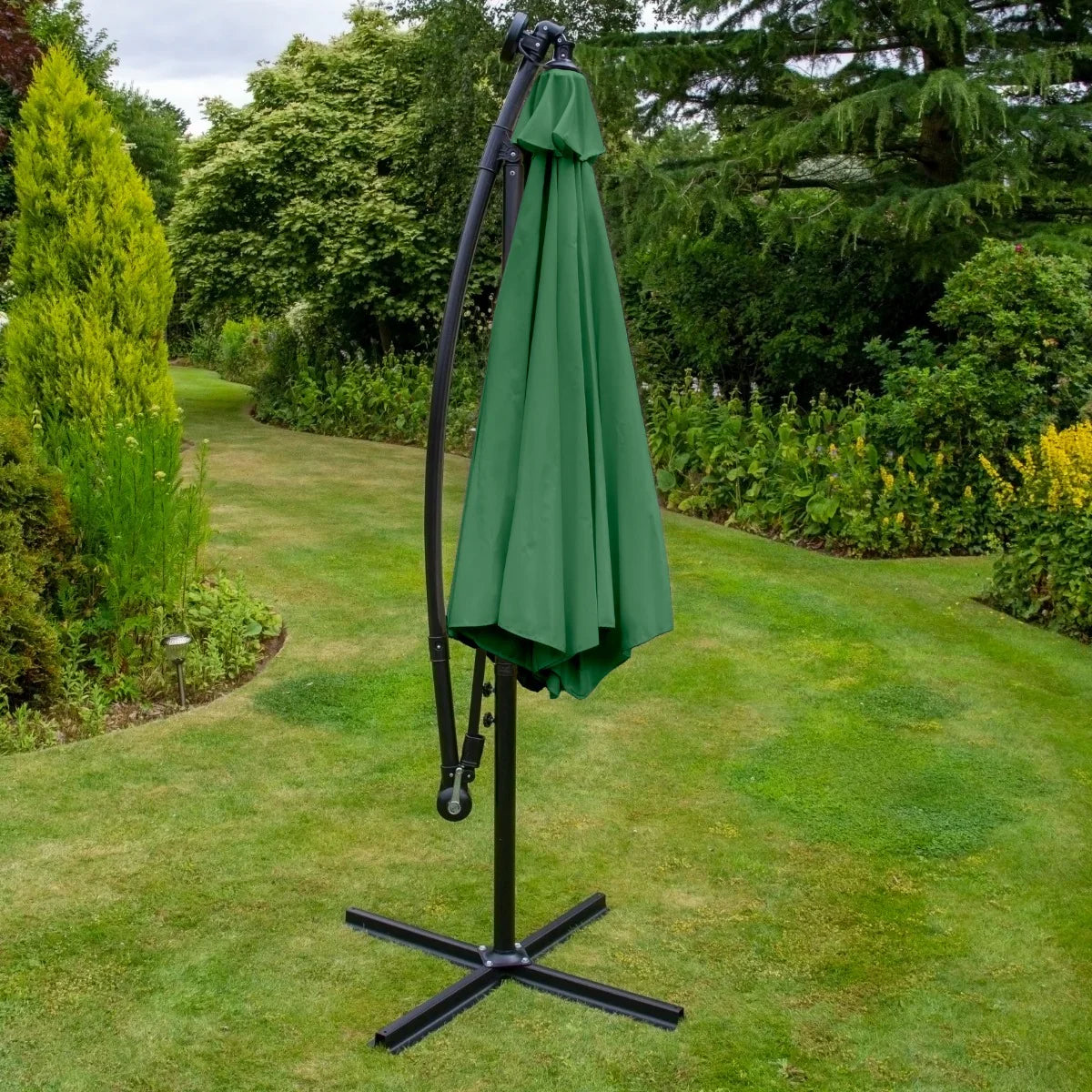 Green 3m LED cantilever parasol with a curved frame and fabric canopy, standing on a sturdy black base in a lush garden setting
