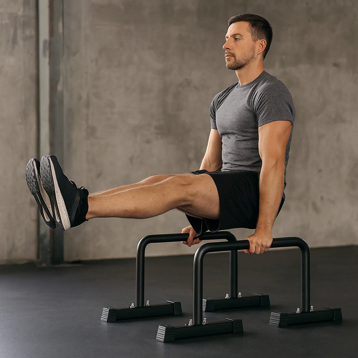 Large parallettes in use by a man in a gray shirt and black shorts, demonstrating strength training with elevated leg holds on a smooth floor