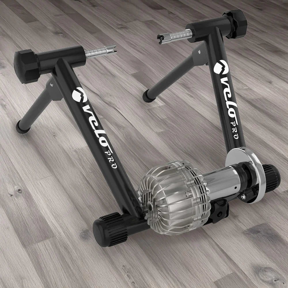 Black Velo Pro Fluid Turbo indoor bike trainer with a sleek silver resistance unit and sturdy black frame on a wooden floor