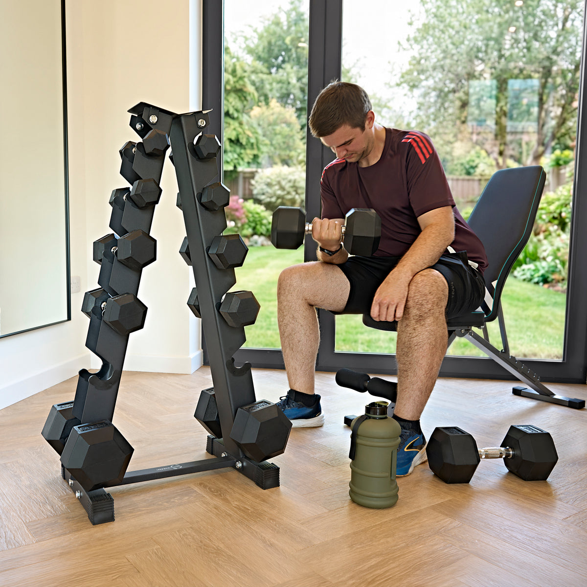 Black hex dumbbell rack with six tiers, holding various weights, alongside a man lifting a dumbbell in a modern home gym setting