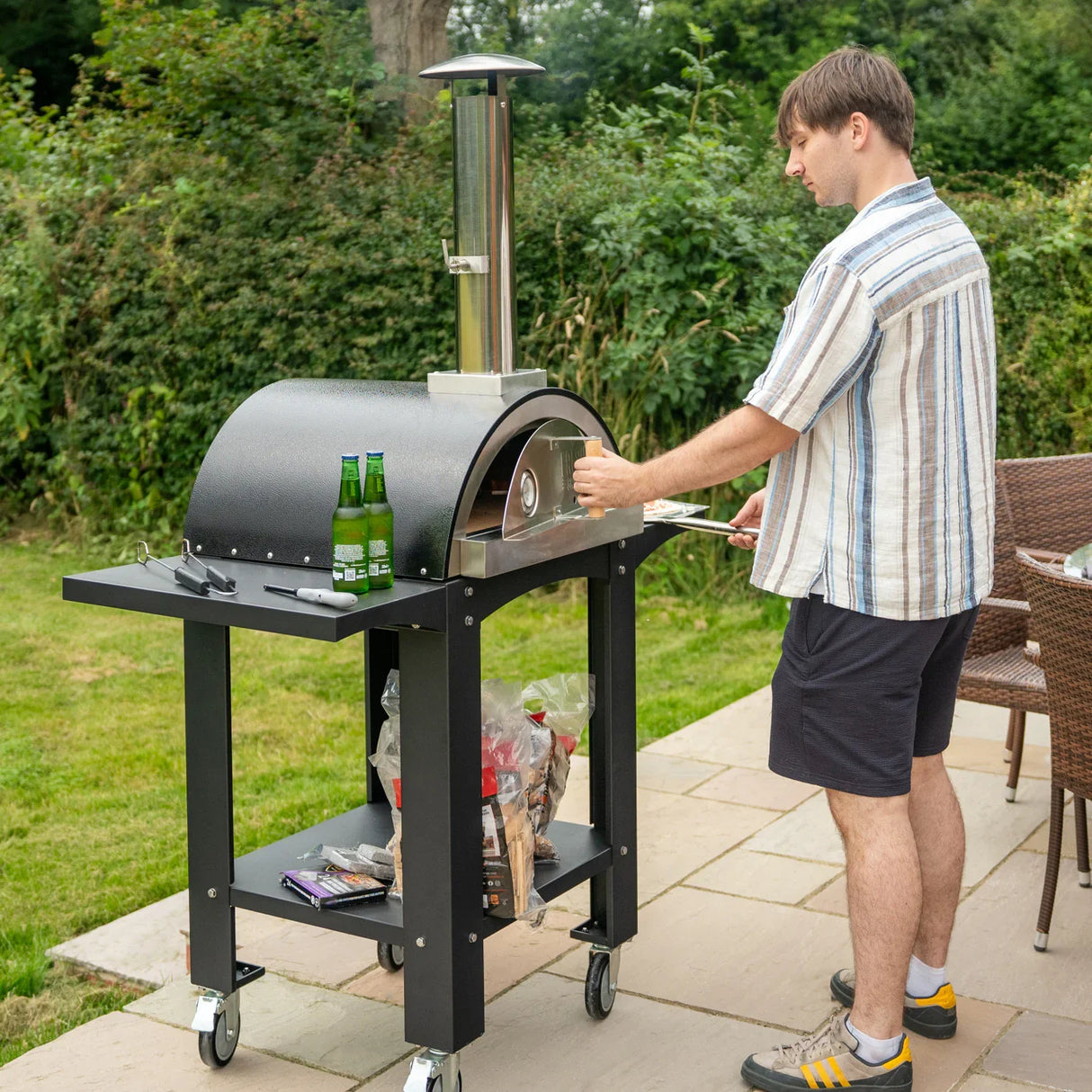 Extra large free-standing pizza oven with a sleek black finish, prep stations, and a man placing a pizza inside on a patio