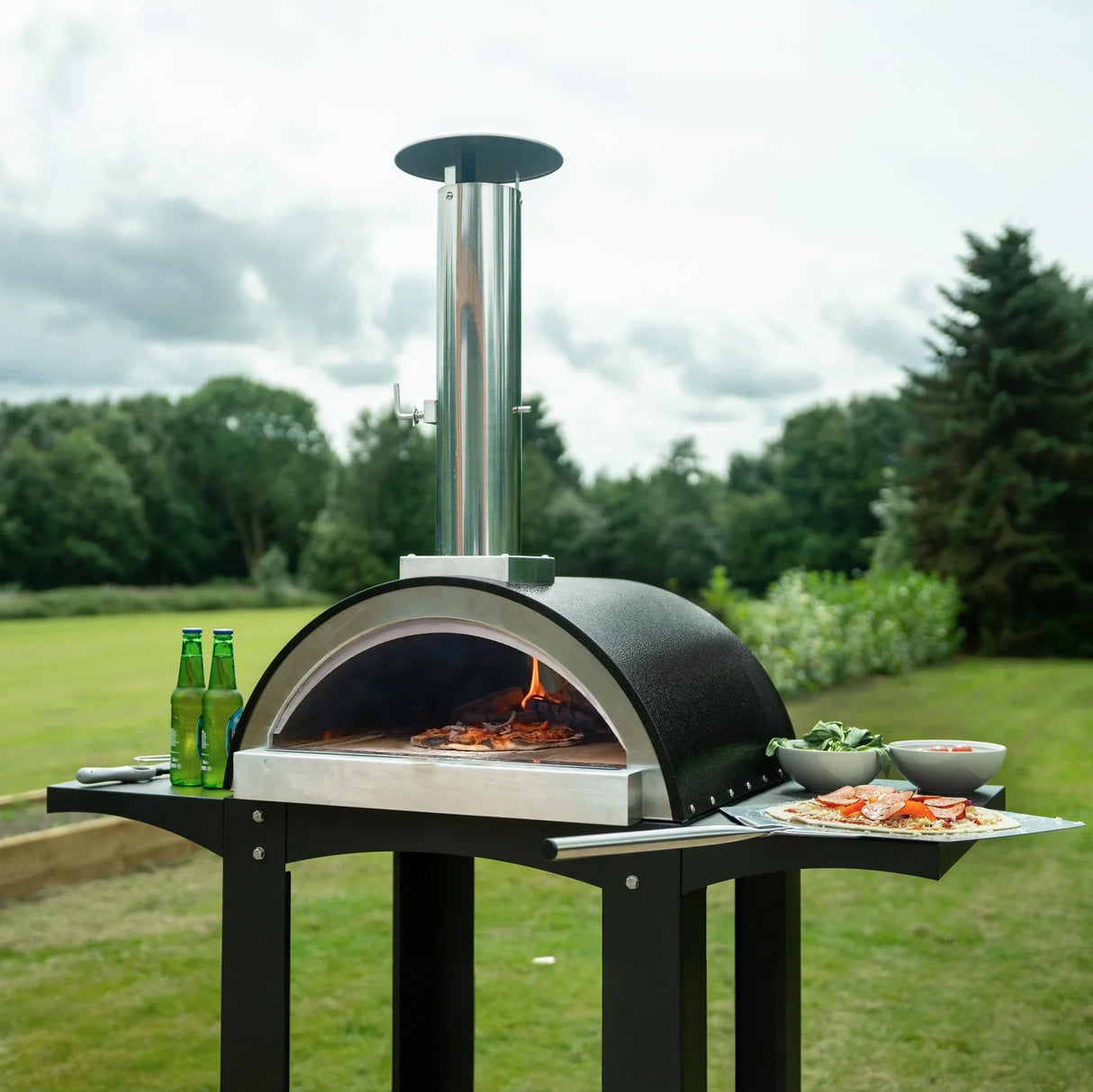 Extra large free-standing pizza oven with a sleek black dome, stainless steel chimney, and prep stations for outdoor cooking