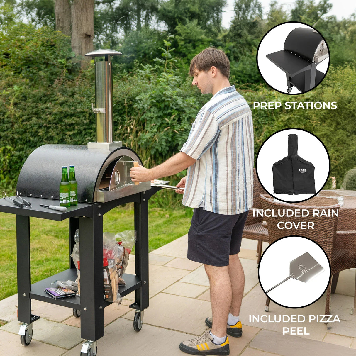 Extra large free-standing pizza oven with black finish, prep stations, and included rain cover, set on a patio with drinks nearby