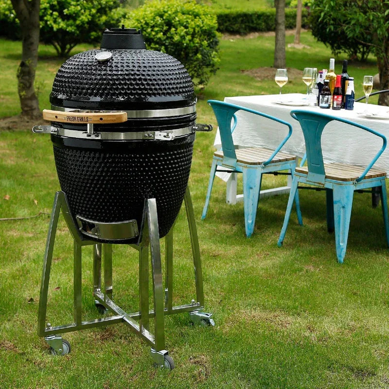 Fresh Grills Kamado Charcoal BBQ Grill 21" in black with textured surface, set outdoors beside a dining table and chairs