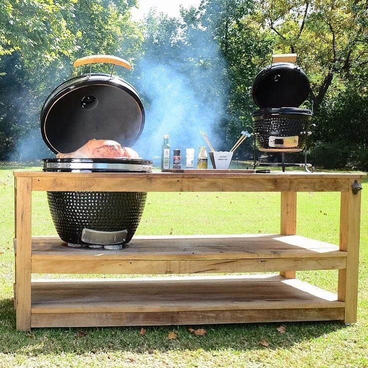 Fresh Grills Kamado Charcoal BBQ Grill 21" in black with smoke, set on a wooden table outdoors, showcasing grilling accessories and food