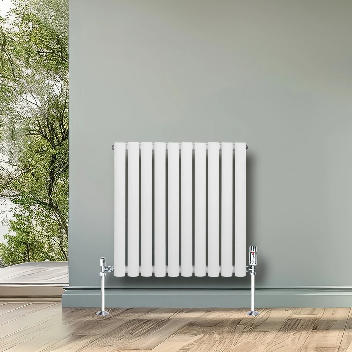 White oval single column radiator with chrome valves, 600mm x 600mm, mounted on a wall in a bright, modern room with wooden flooring