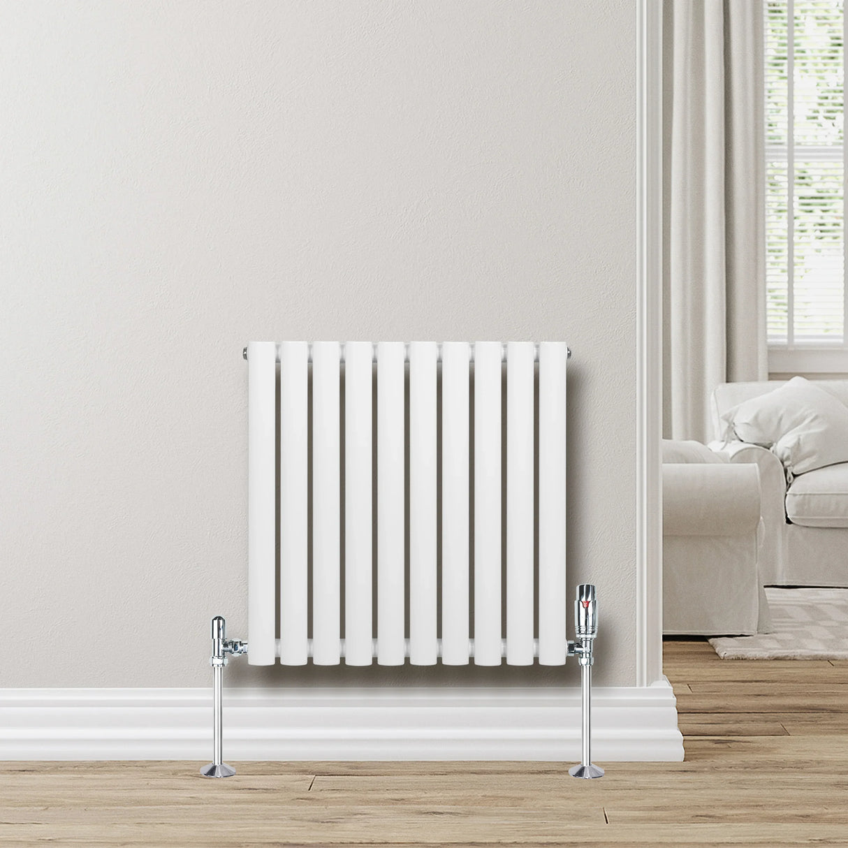 White oval single column radiator with chrome valves, 600mm x 600mm, mounted on a light-colored wall in a cozy room setting