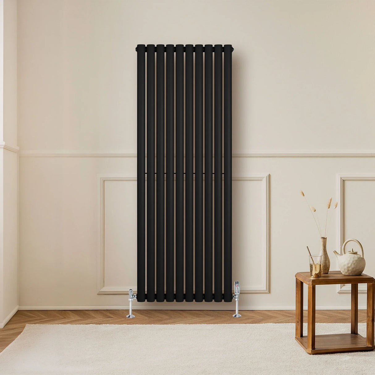 Sleek black oval single column radiator with vertical bars, complemented by chrome valves, set against a neutral wall and wooden floor