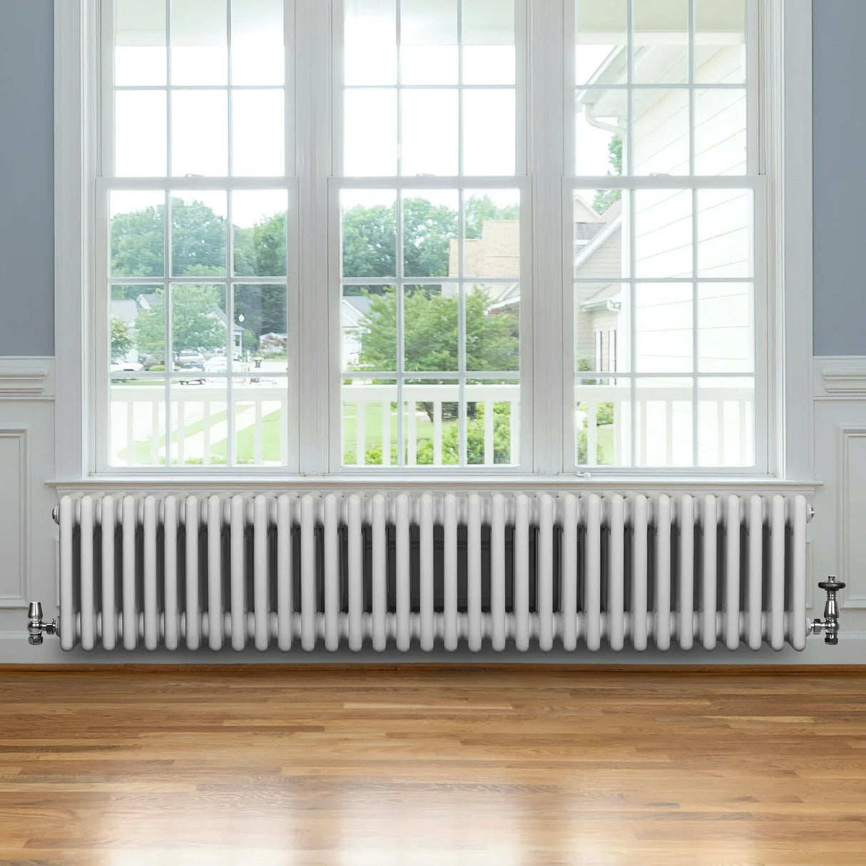 Traditional white 4 column radiator with valves, featuring a sleek design and smooth finish, positioned under a large window