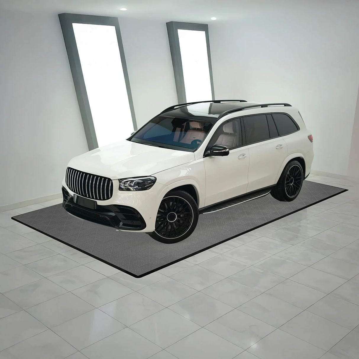 Vented grey garage floor tiles arranged under a sleek white SUV, showcasing a modern, textured design in a spacious setting