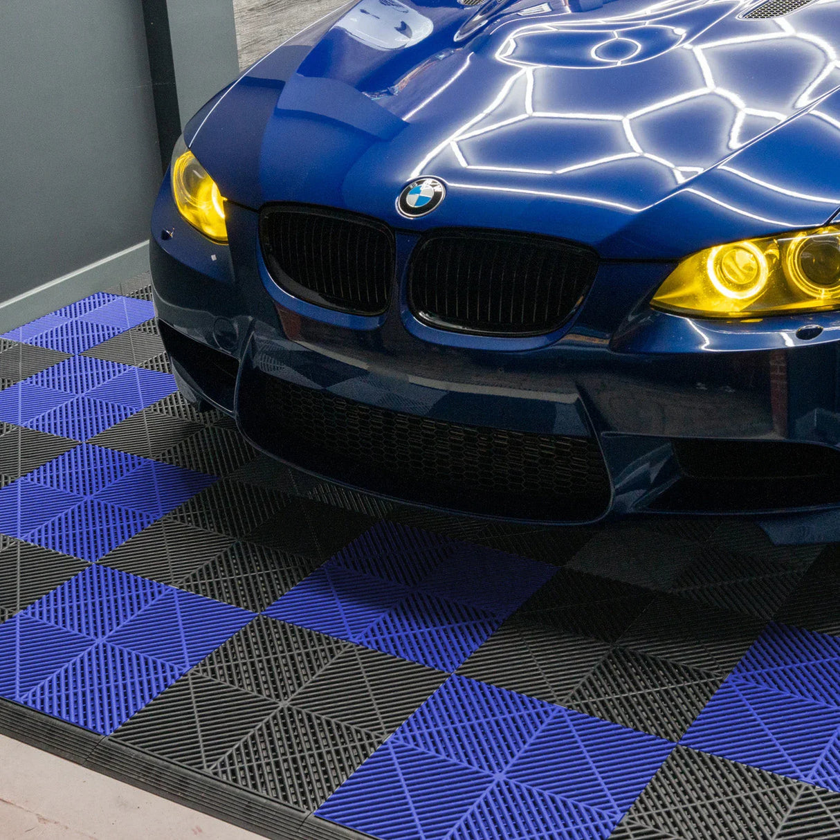 Vented garage floor tiles in black and blue, featuring a textured surface, arranged in a checkerboard pattern under a sleek blue car