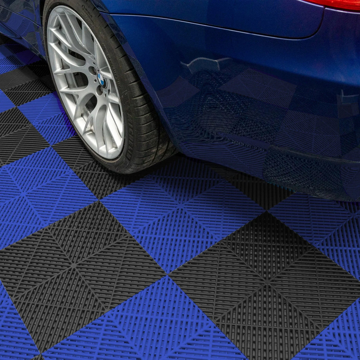 Vented garage floor tiles in black and blue, featuring a textured surface, arranged in a checkerboard pattern beneath a blue car