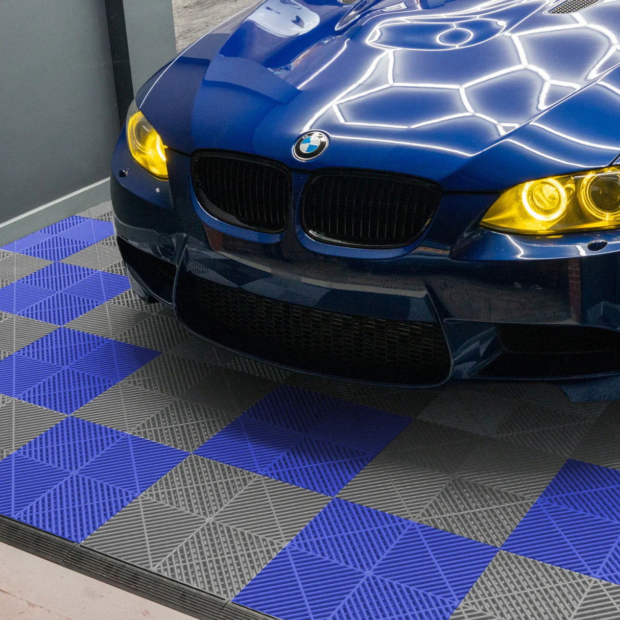 Vented garage floor tiles in grey and blue, featuring a textured surface, arranged under a sleek blue BMW sports car