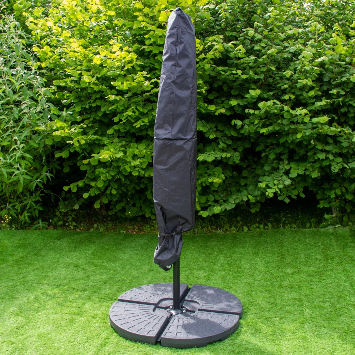 Green 3m LED cantilever parasol with a sturdy fan base, featuring a protective cover, set against lush greenery on grass