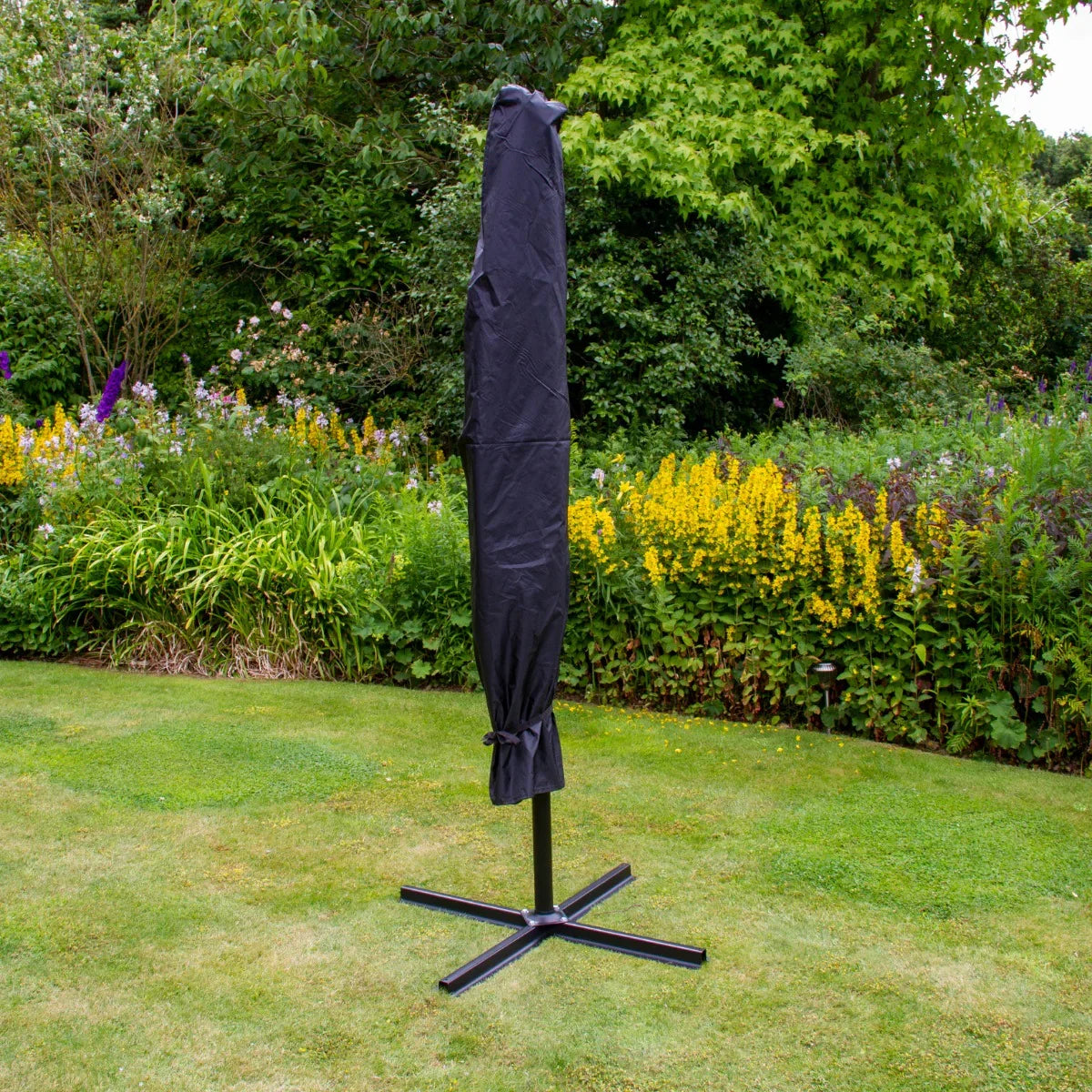 Grey 3m LED cantilever parasol in protective cover, standing on a black base, surrounded by vibrant garden flowers and greenery