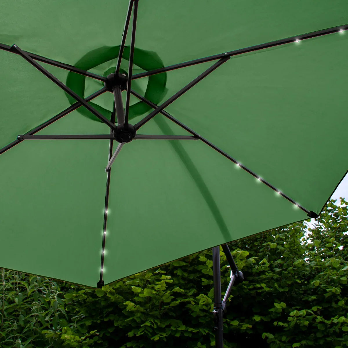 Green 3m LED cantilever parasol with a sturdy black frame, showcasing bright LED lights along the ribs, set against lush greenery