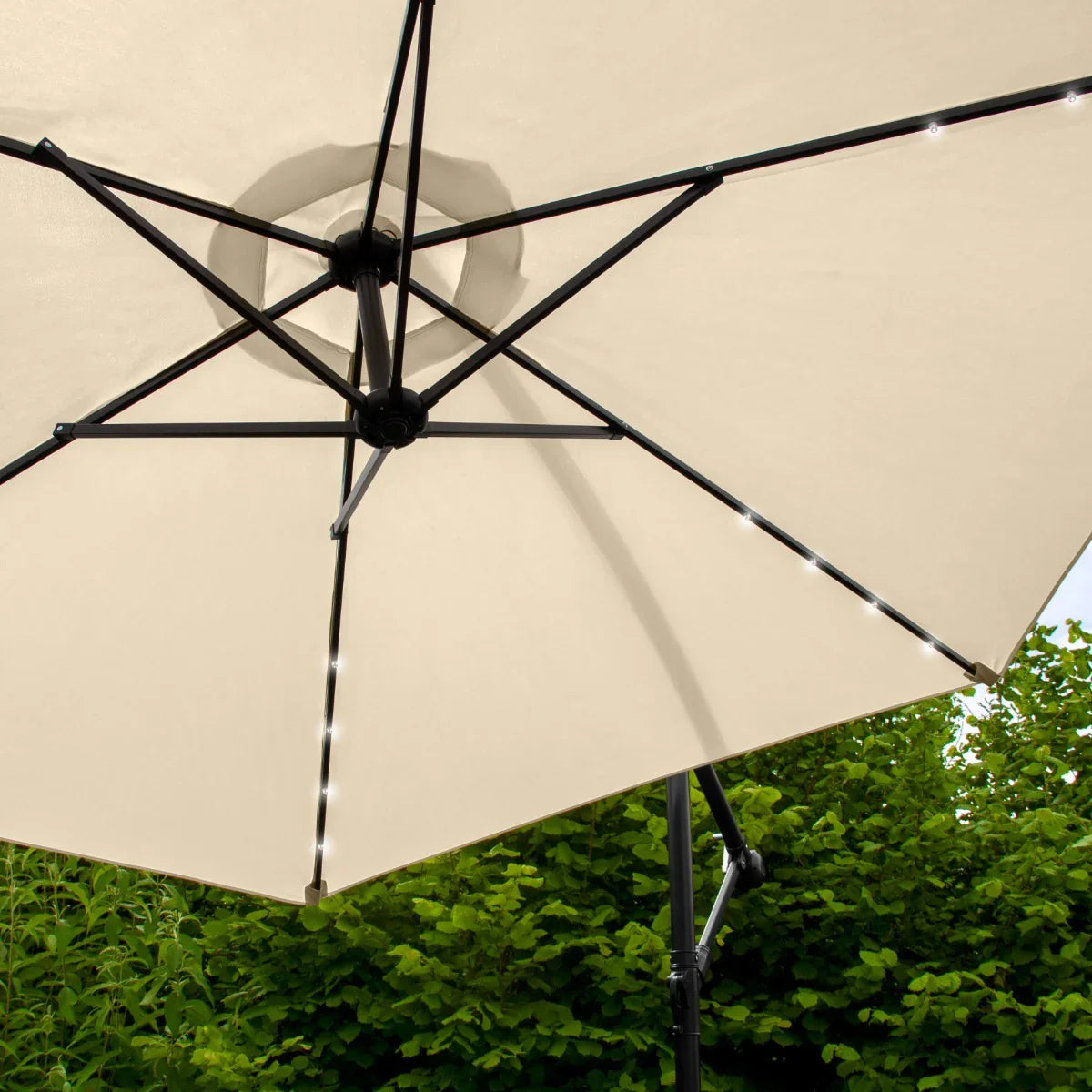 Beige 3m LED cantilever parasol with a sturdy black frame, showcasing illuminated edges and a spacious canopy against greenery