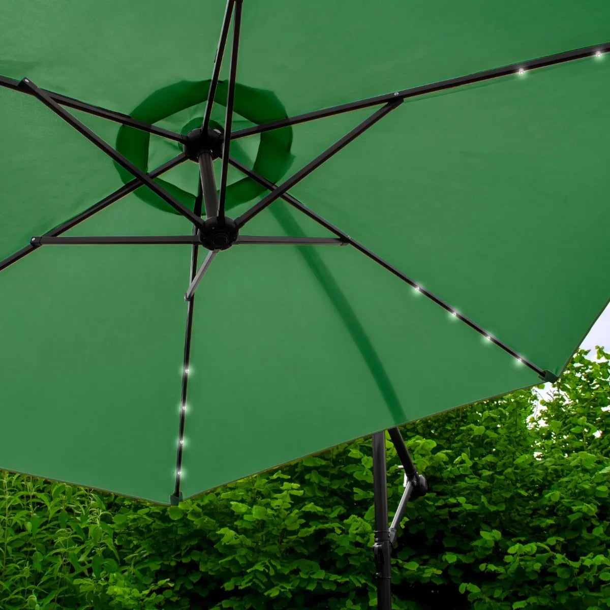 Green 3m LED cantilever parasol with a sturdy black frame, featuring soft glowing lights along the ribs, set against lush greenery