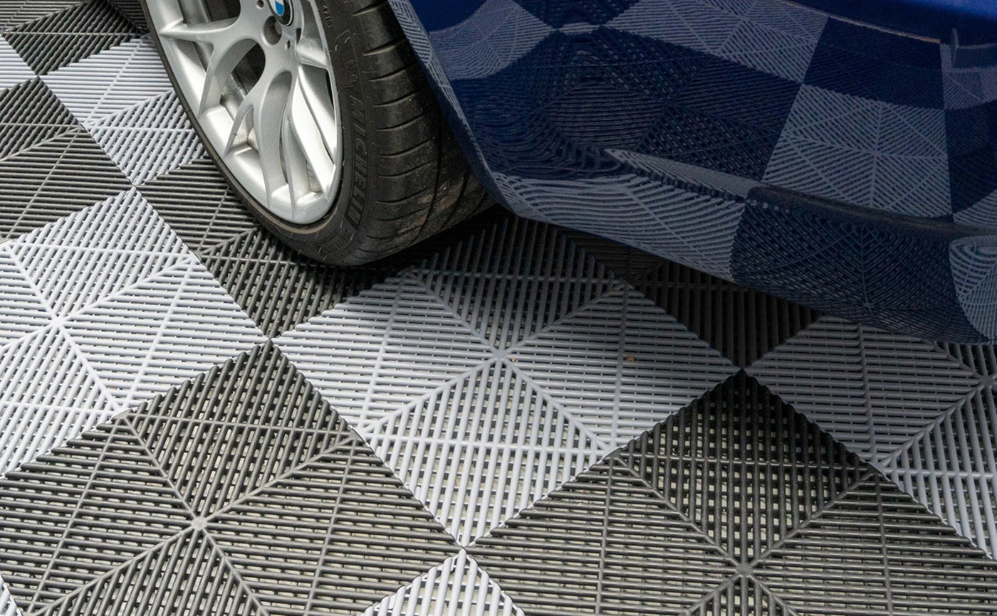 Close-up of a car tire on a textured gray and black checkered floor mat, showcasing its geometric pattern and durable material