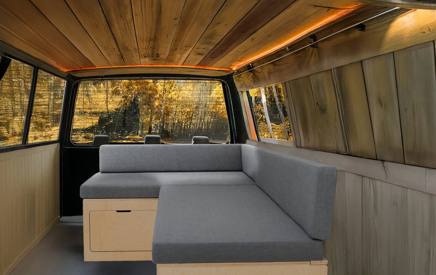 Cozy van interior featuring light wood paneling, gray cushioned seating, and warm ambient lighting, perfect for travel and relaxation
