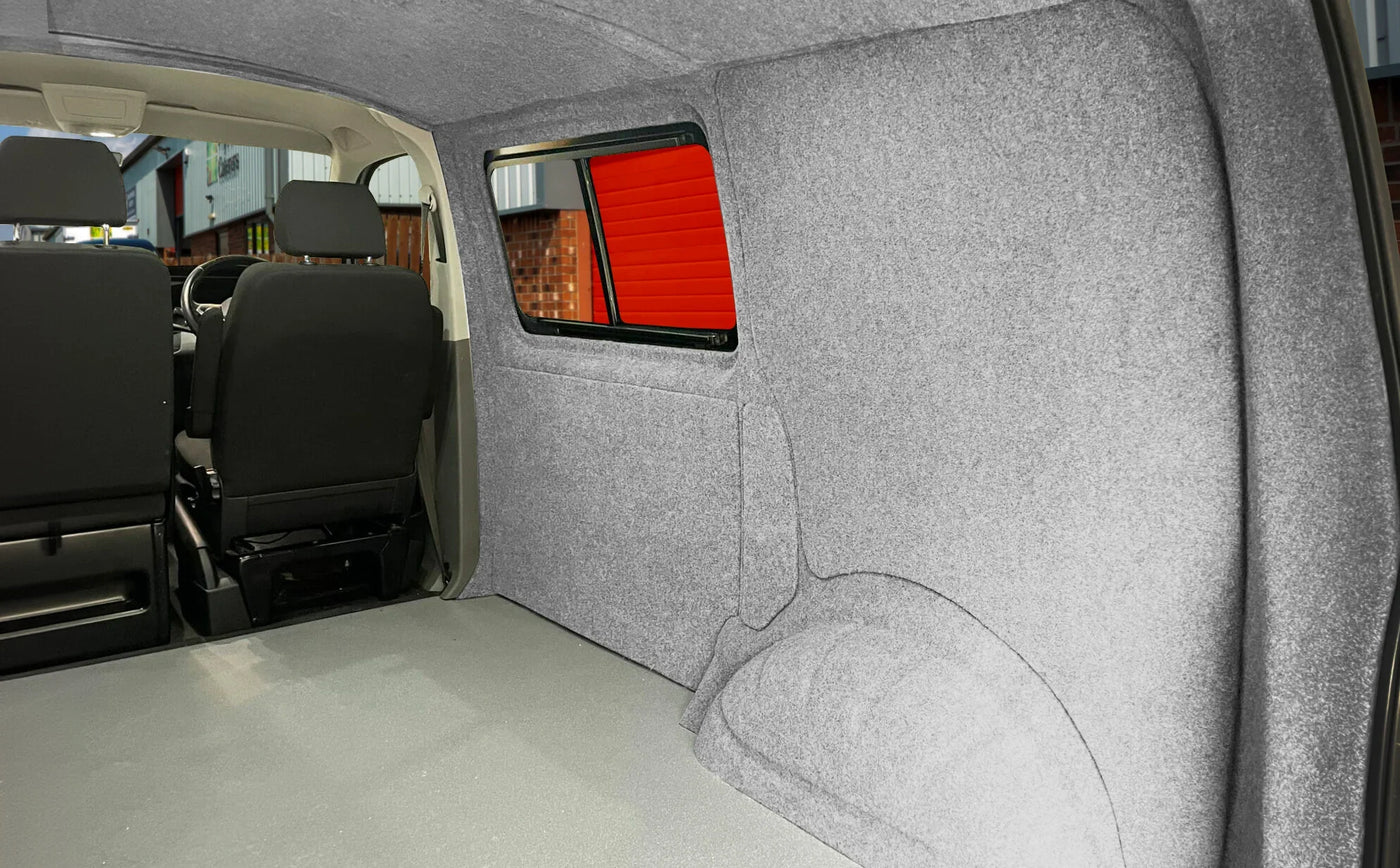 Interior of a van featuring gray felt lining, spacious cargo area, and black seating, with a bright red window frame in the background