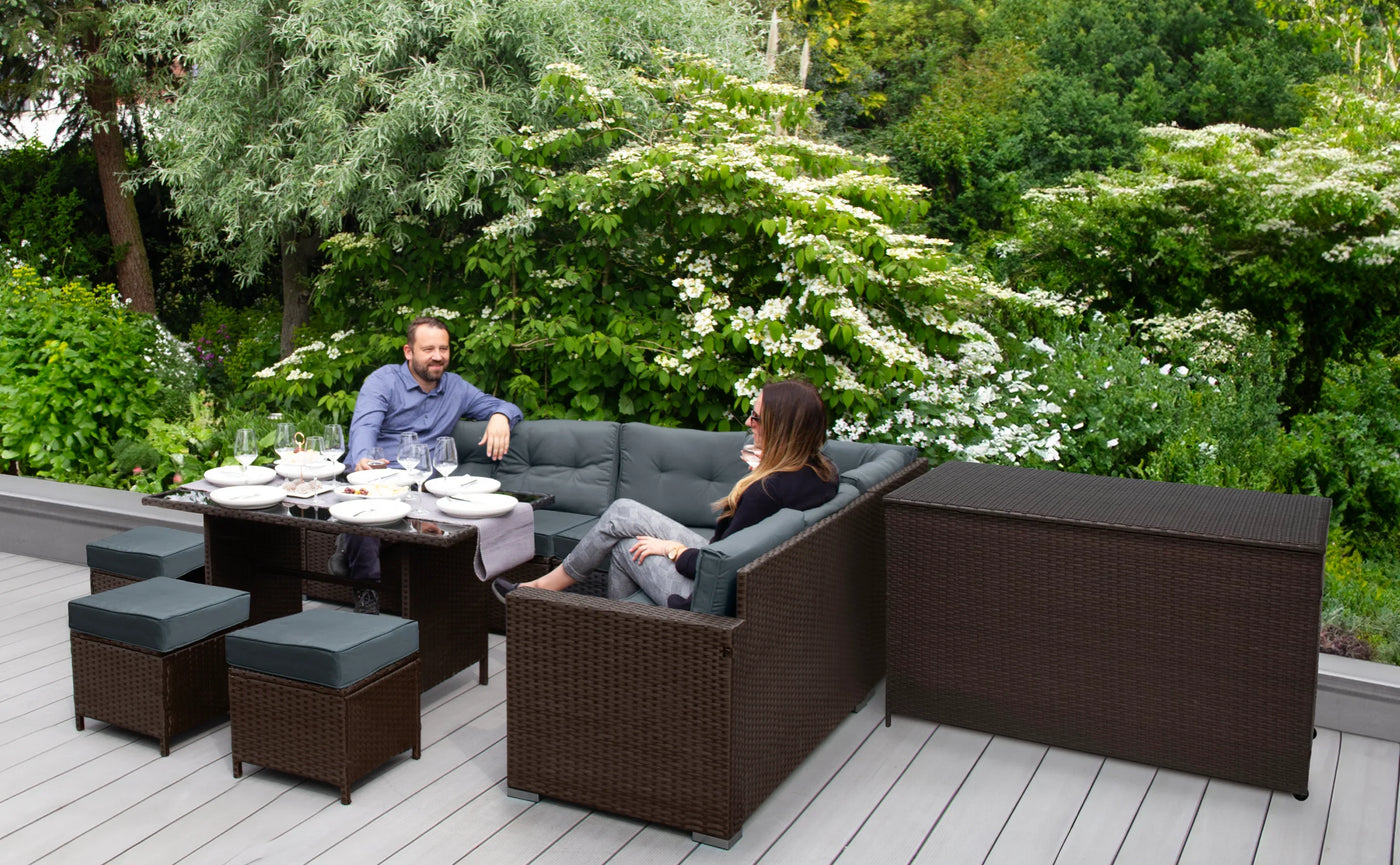 Stylish outdoor seating area with a dark wicker sofa, table, and chairs, surrounded by lush greenery and blooming flowers