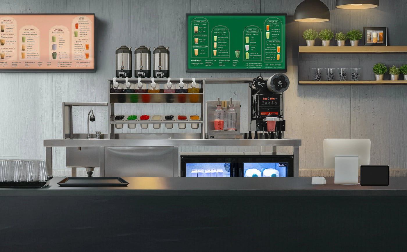 Modern café counter featuring colorful drink dispensers, menu boards, and stylish decor with green plants and sleek appliances