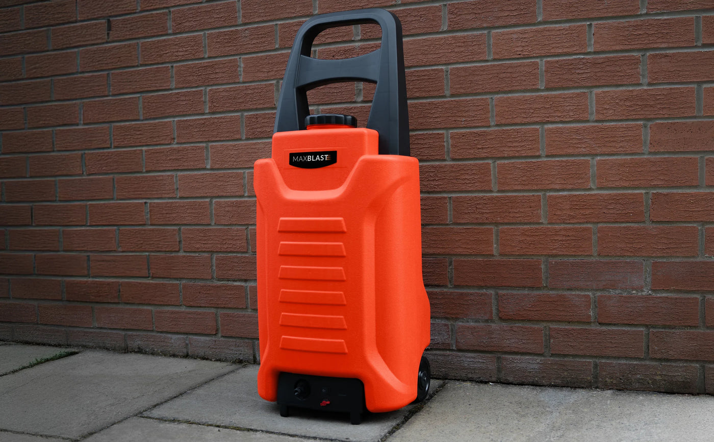 Bright orange portable pressure washer with a sturdy black handle, set against a textured brick wall, showcasing its compact design and wheels