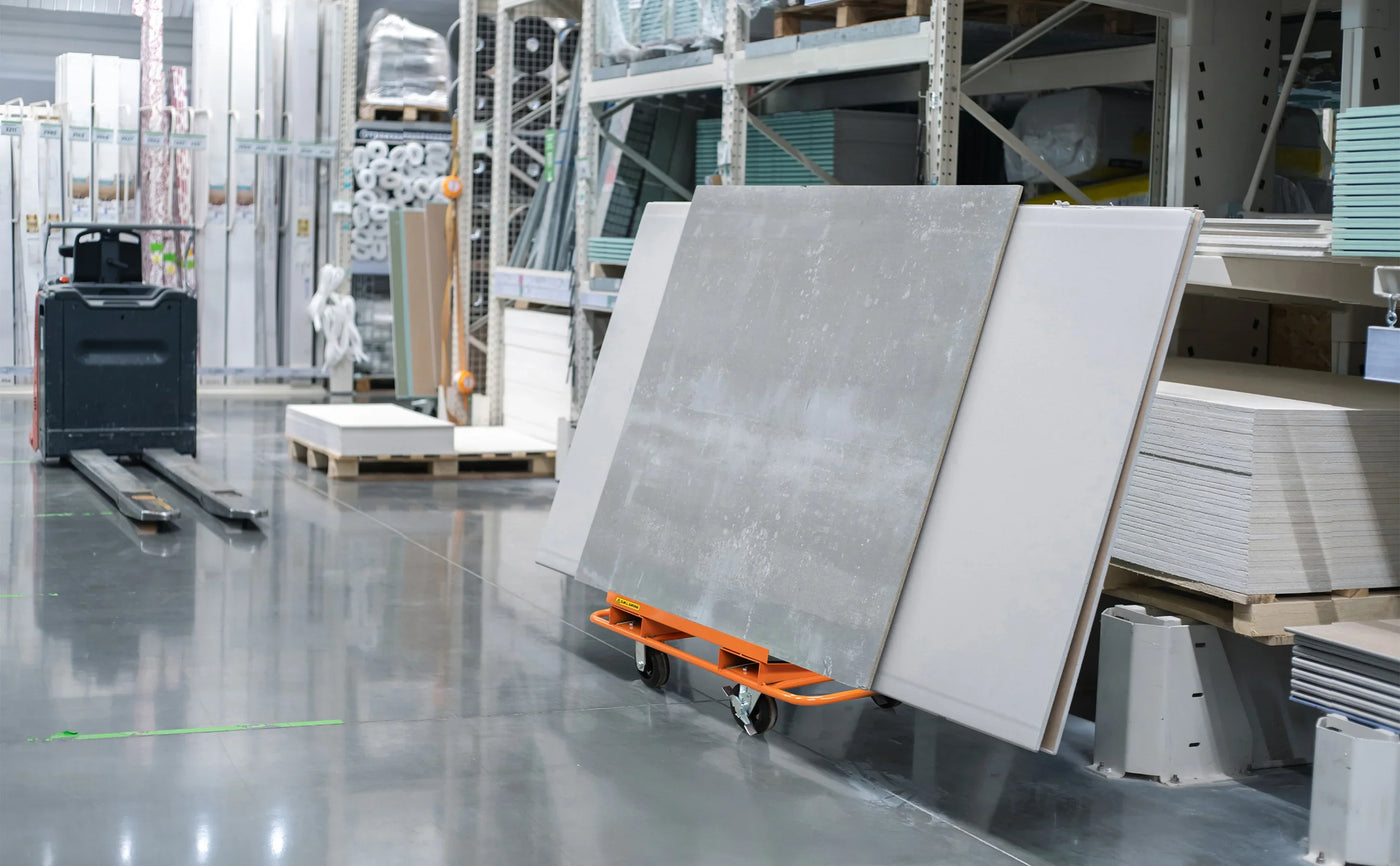 Gray concrete panels on an orange cart in a well-lit warehouse aisle, surrounded by stacks of materials and tools